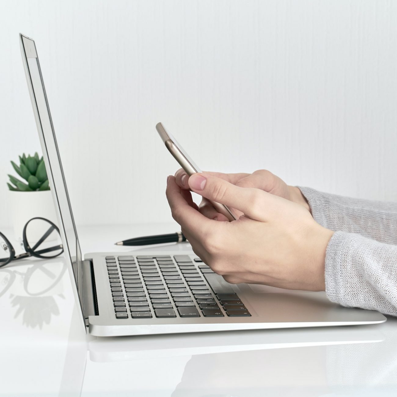 Unrecognizable woman using smartphone while typing on laptop, concept of password entry